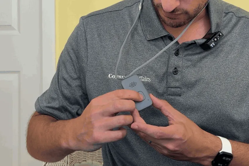 Thumb pressing the Lifeline On the Go pendant's help button until the light turns solid blue