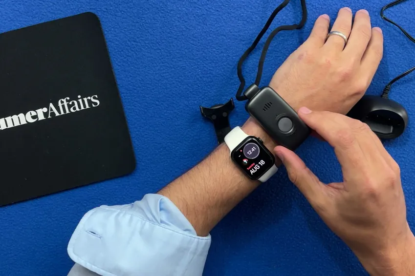 Belle X2 pendant held on a wrist next to an Apple Watch for size, beside a ConsumerAffairs mousepad