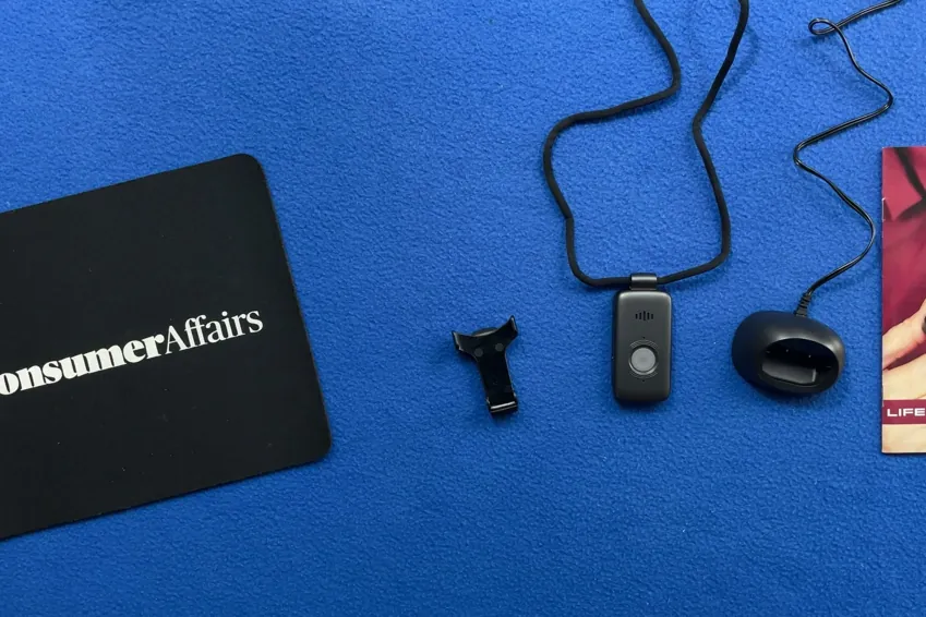 Overhead view of the Belle X2 pendant on its lanyard, charging cradle, belt clip and user guide beside a ConsumerAffairs mousepad