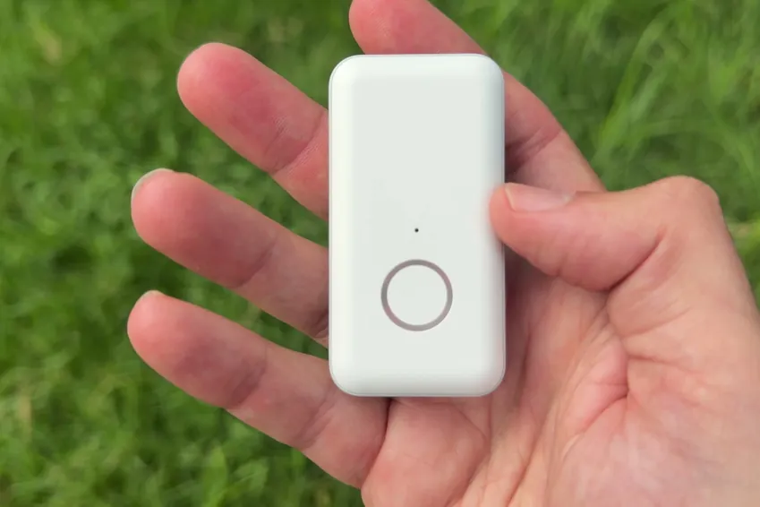 LifeStation Pearl pendant held in an open palm outdoors over grass