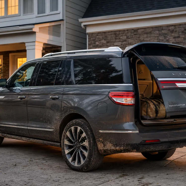 gray SUV with open trunk parked in a driveway outside a house at dusk