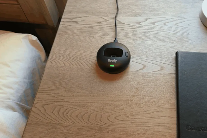 Hand setting the Lively Mobile2 pendant into its charging dock on a nightstand