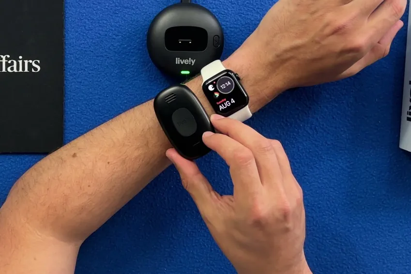 Lively Mobile2 pendant held on a wrist next to an Apple Watch for size