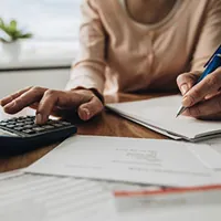close up of a person using a calculator with one hand and writing something on a notebook with the other hand