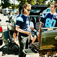 smiling friends wearing team jersey barbecuing in a stadium parking lot