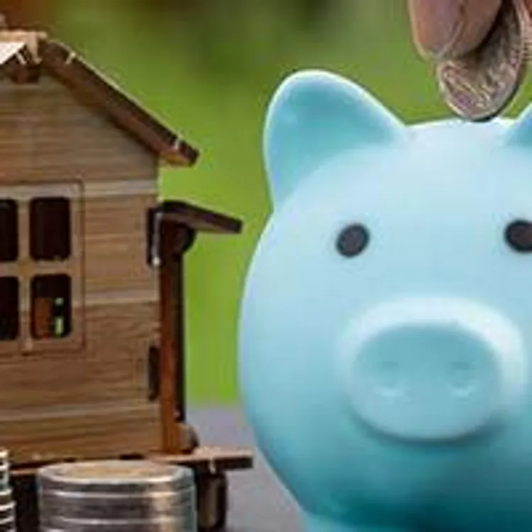 man putting coin in piggy bank next to stacked coins and model home