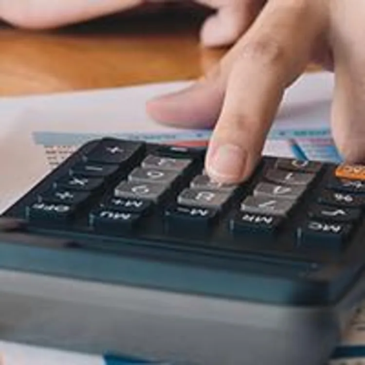man typing on calculator next to model home