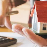 man using calculator holding model home