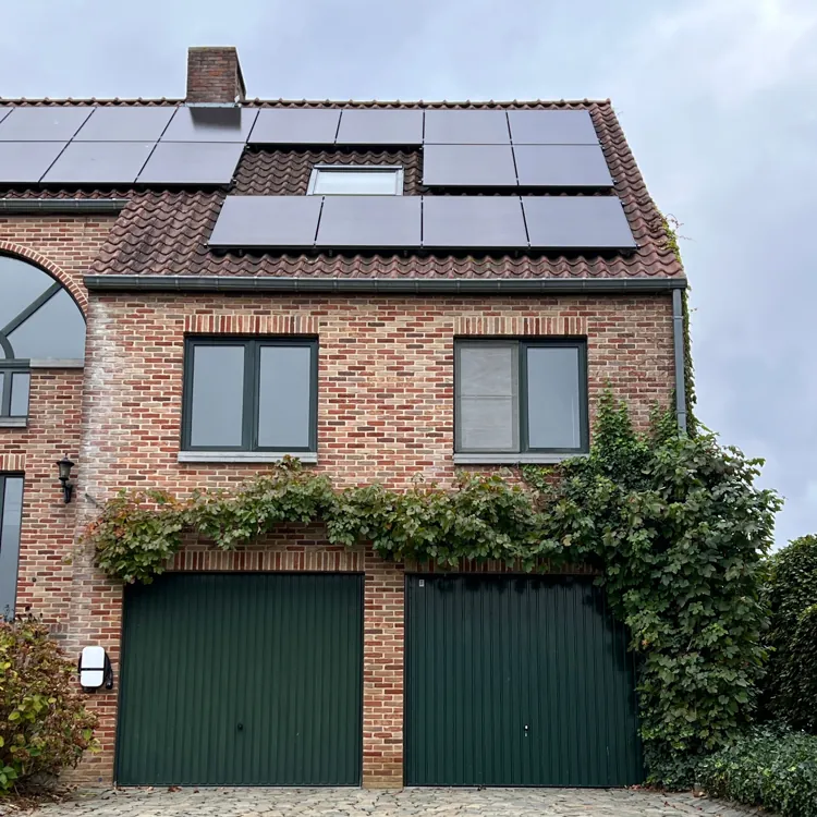Brick house with solar panels on roof, green garage doors, and climbing vines