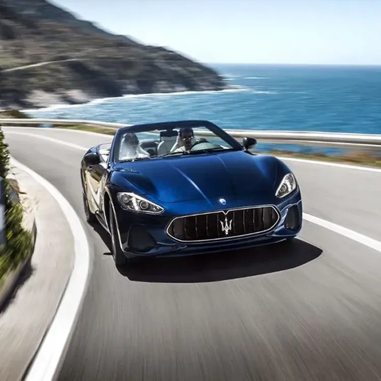 Blue convertible sports car driving on a winding coastal road with ocean in the background