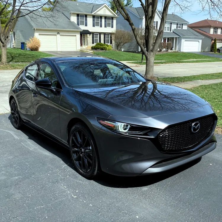 Gray car parked on a suburban driveway with houses and trees in the background on a clear day.