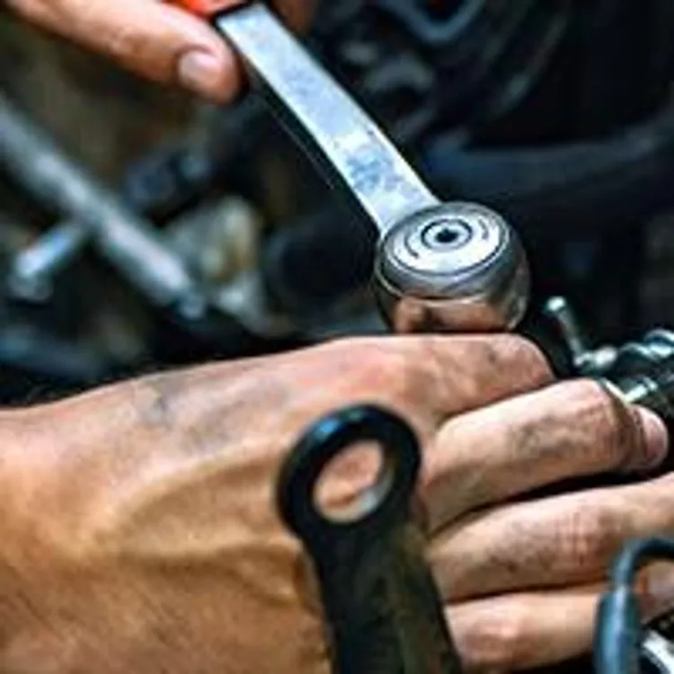hands of car mechanic working on engine with a wrench