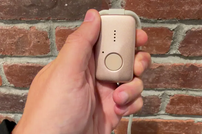 Rose gold MGMini pendant held in a hand in front of a brick wall