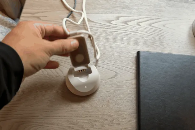 Hand setting the MGMini pendant into its charging base on a bedside table until the orange light comes on