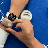 Finger pressing the MGMini help button until it lights green, next to an Apple Watch