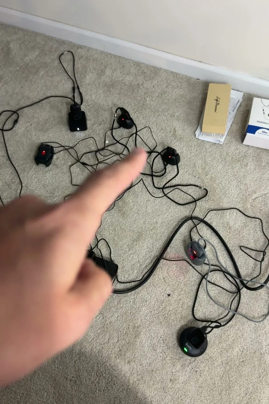 A finger pointing at pendants charging in a tangle of cables on the carpet