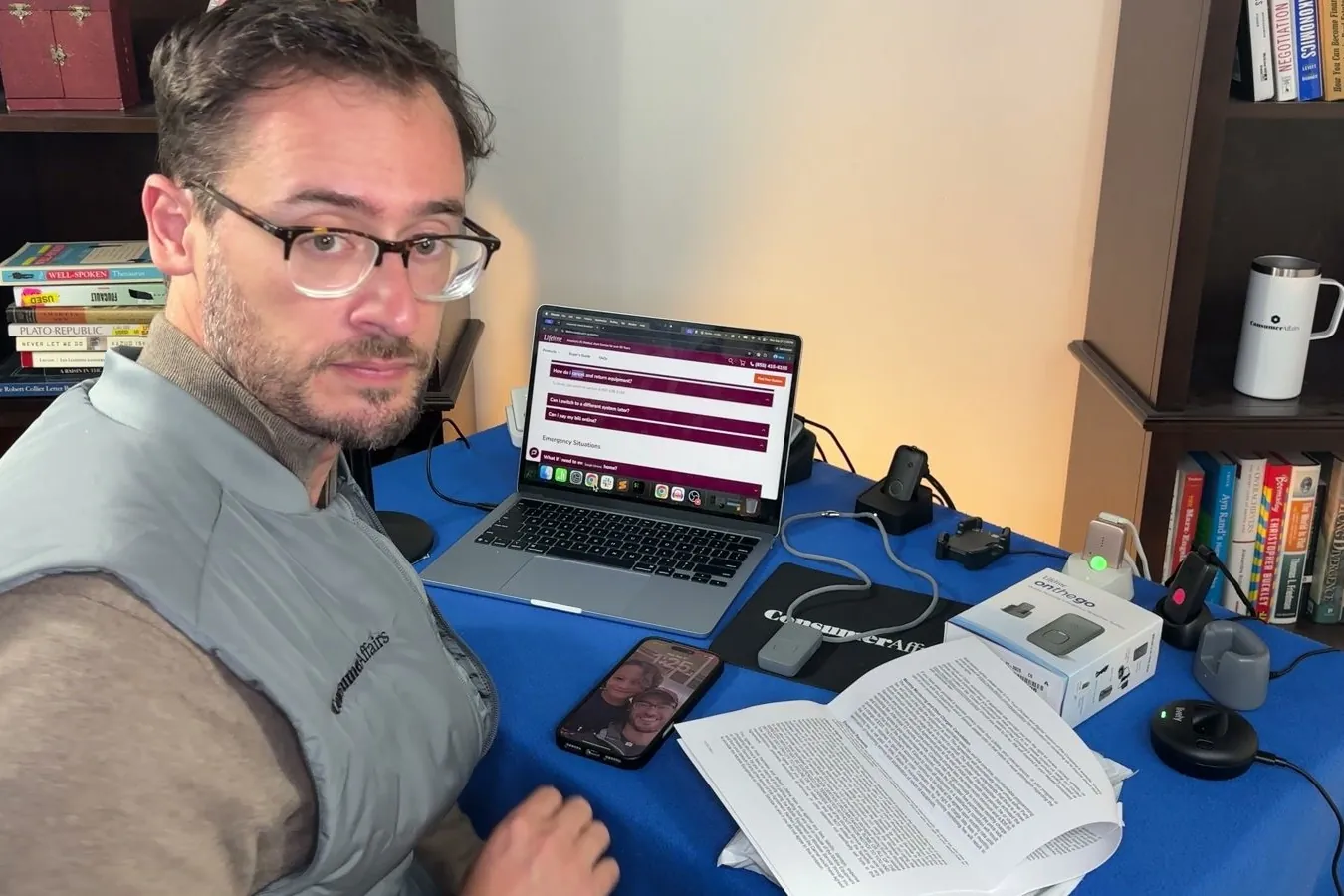 Chris at his desk turning toward the camera, a contract and a device box in front of him