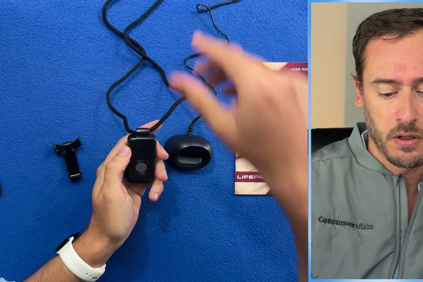 Hands holding a small medical alert pendant and its charging cradle on a blue table