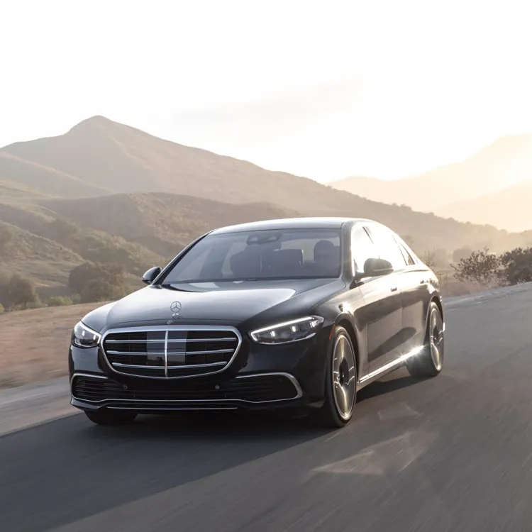 Black luxury sedan driving on a paved road with hills and trees in the background