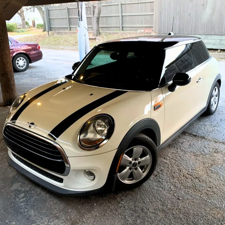 White Mini Cooper with black racing stripes parked in a covered garage.