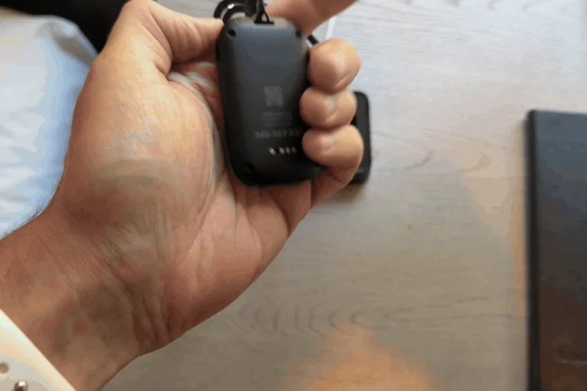 Hand setting the MobileHelp Elite pendant into its charging dock on a nightstand
