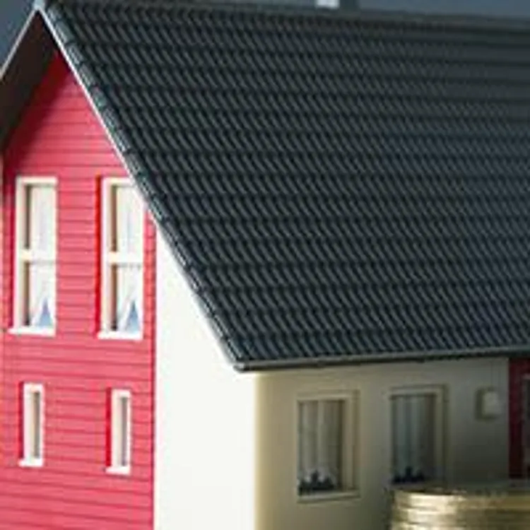 miniature house behind three stacks of coins beside a porcelain piggybank