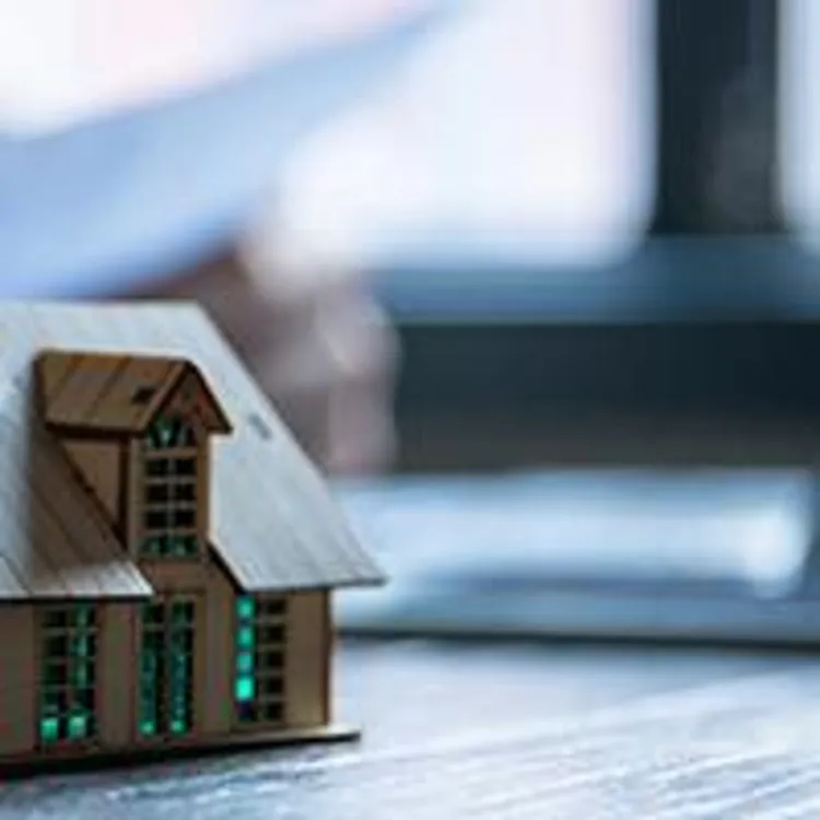 small home with keys in the foreground while woman looks over paperwork in the background