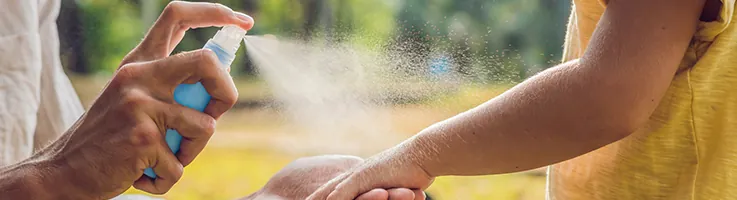 mom spraying mosquito repellent on child