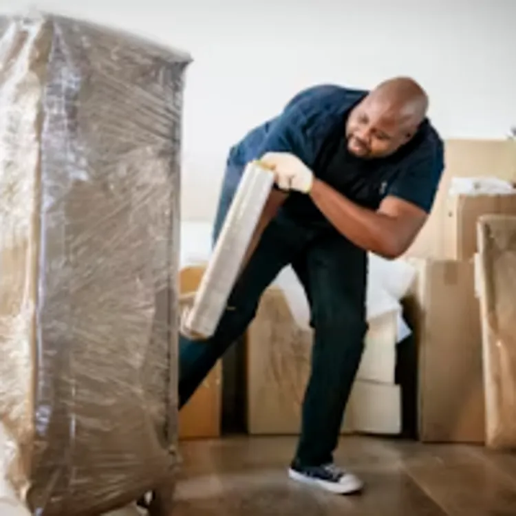 Man moving wrapped furniture and boxes in a home with wooden floors