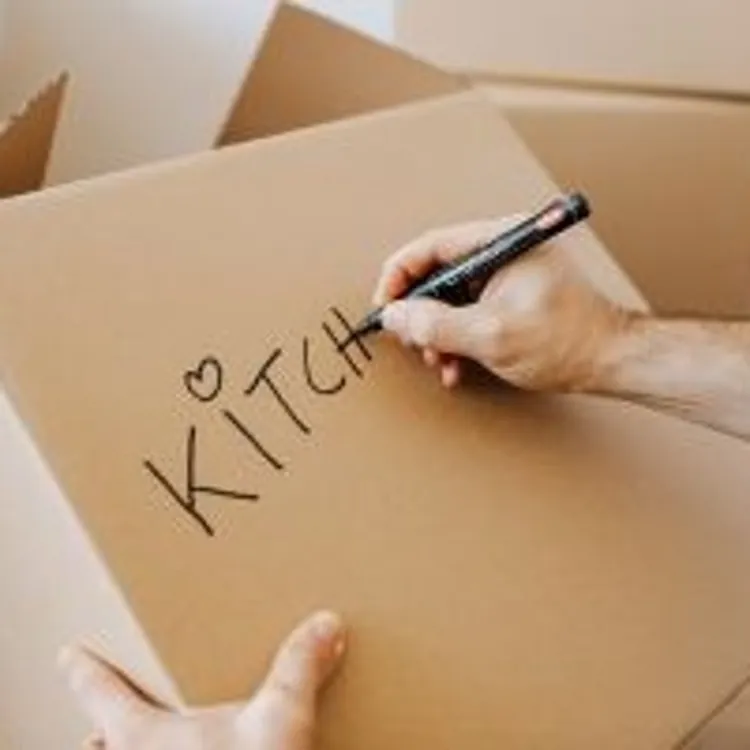 Person labeling a cardboard box kitchen with a marker