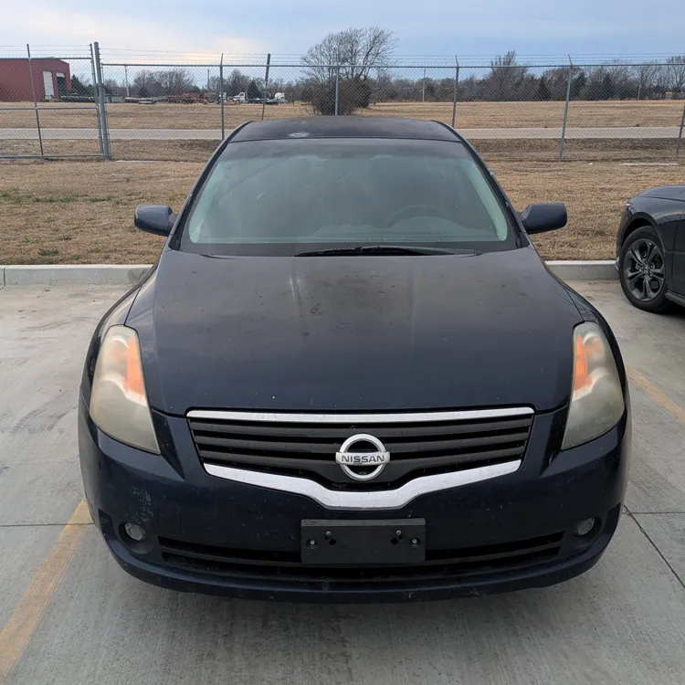 Front view of a black Nissan car parked in an outdoor parking lot on an overcast day.