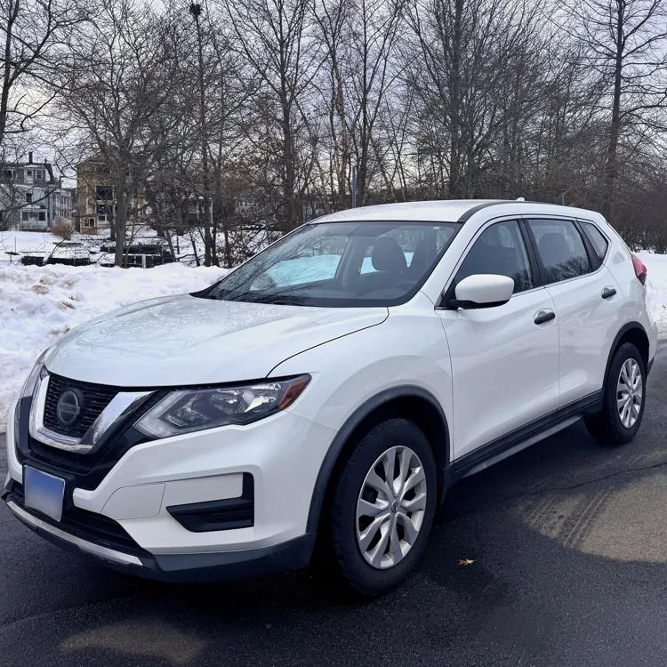 White SUV parked on a snowy road with bare trees and an overcast sky in the background.