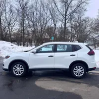 White SUV parked on a wet road with snow piled on the sides and bare trees in the background.