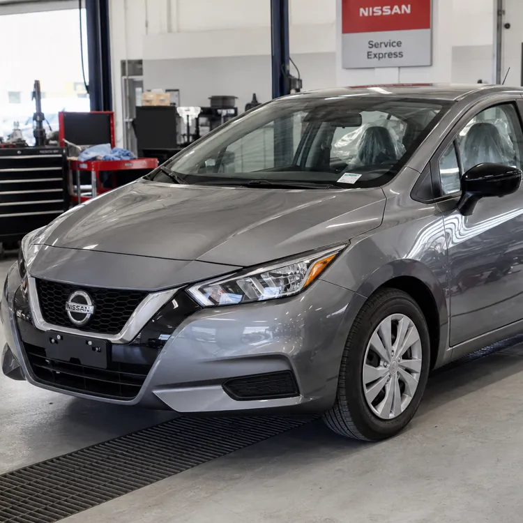 Gray Nissan sedan parked inside a service garage with tools and equipment nearby