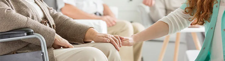older lady in a wheelchair being comforted by a nurse