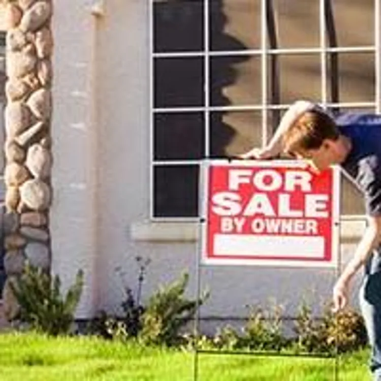 owner putting for sale sign in front of home