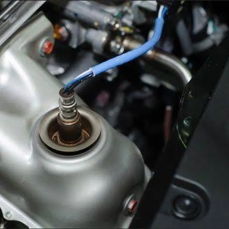 An oxygen sensor with a blue wire is installed in a car engine compartment.