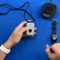 Man at desk with medical alert device, wristband, and charging dock on blue surface