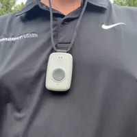 Person wearing a medical alert device on a lanyard over a black shirt outdoors