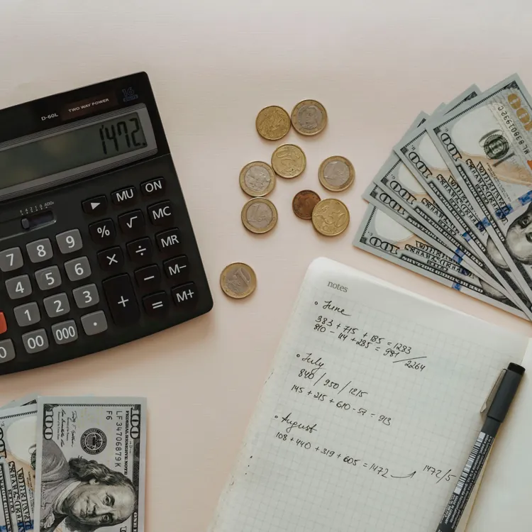 Calculator, US dollar bills, coins, and a notebook with handwritten calculations on a table