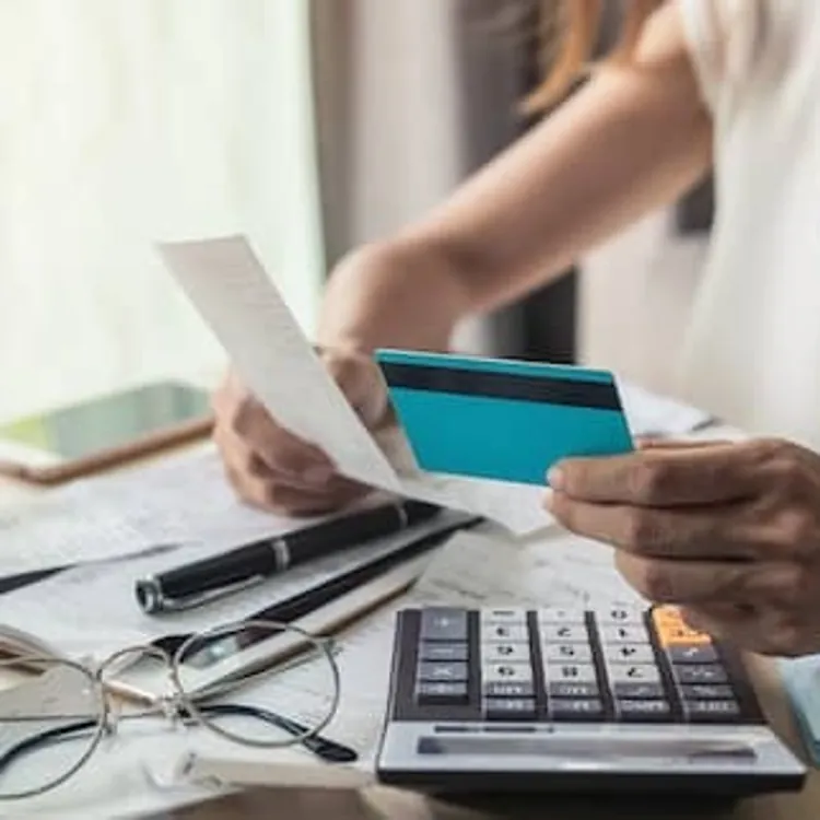 Person holding a credit card and receipt at a desk with a calculator, papers, and glasses