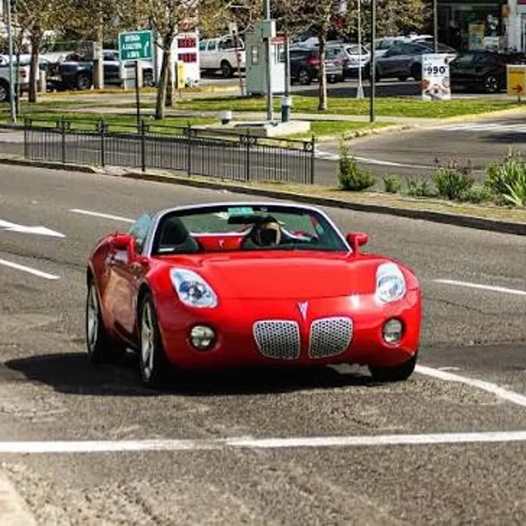 Red convertible car driving on a city street in daylight