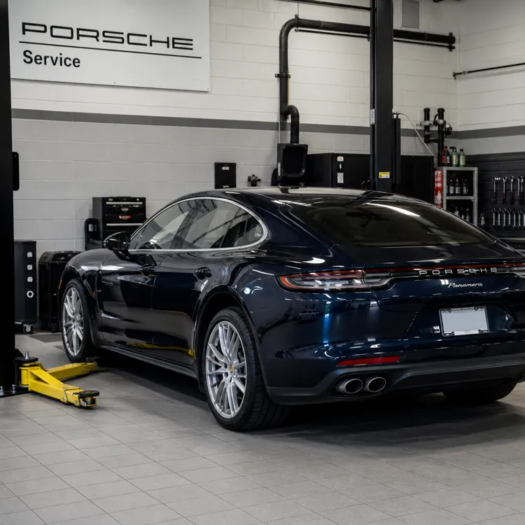 Black Porsche sedan parked in a clean auto repair shop with tools and equipment visible