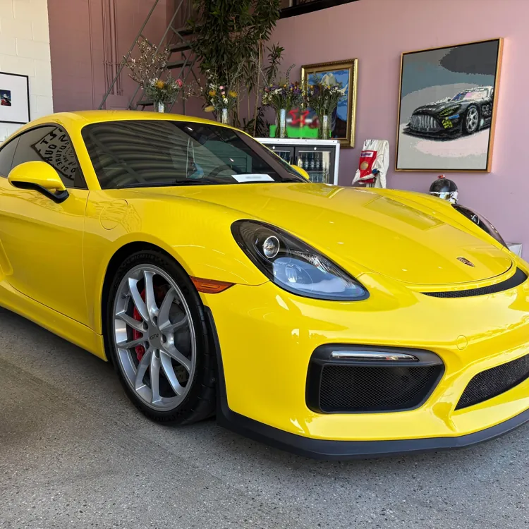 Yellow sports car with sleek design parked in a showroom with art on the walls.