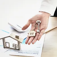 agent offering key to a house, desk and paperwork in background