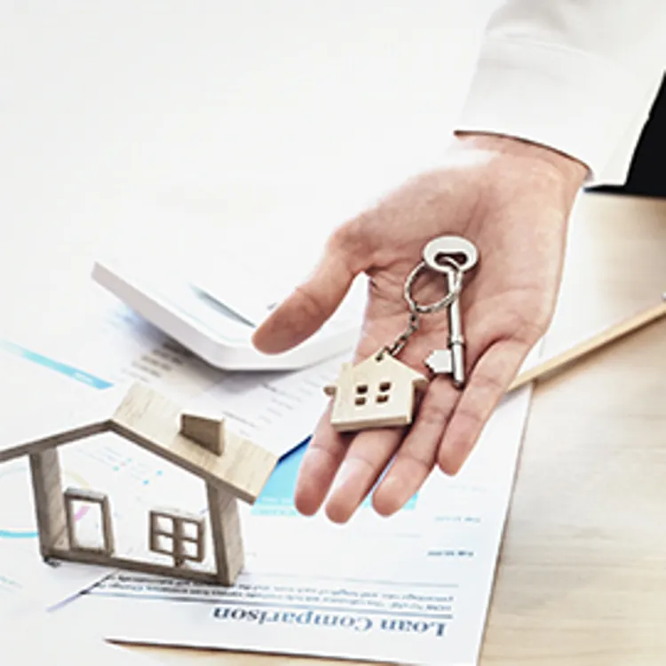 agent offering key to a house, desk and paperwork in background