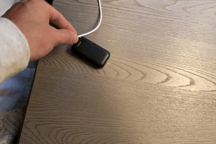 Hand attaching the magnetic charging cable to the SecuLife SOS pendant on a nightstand