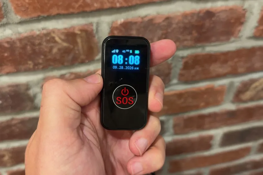 SecuLife SOS pendant held in a hand with its screen showing the time above the red SOS button