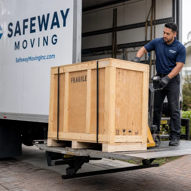Mover unloading a large wooden crate labeled fragile from a Safeway Moving truck at a house