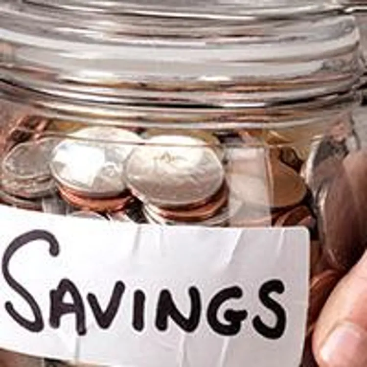 person holding a glass jar full of coins with the label savings on it